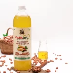 Product photography showcasing a bottle of Vedikpro Cold Pressed Groundnut Oil next to a basket of peanuts on a white background.